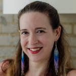 Headshot of Megan Harris. Megan has long brown hair, dark eyes and light skin. She is smiling and wearing blue and purple beaded dangling earrings.