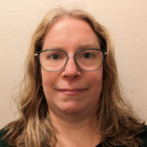 Headshot of Suzanne Aubin. Suzanne has long blond hair and light skin. She is wearing dark-rimmed glasses.