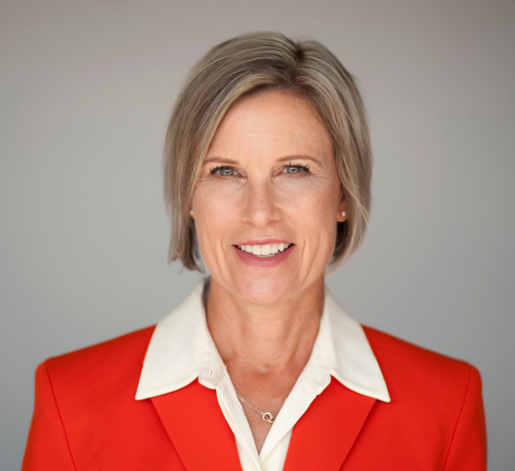 Headshot of Lucy Payette. Lucy has short fair hair, blue eyes, and light skin. She is wearing a red jacket over a white shirt.