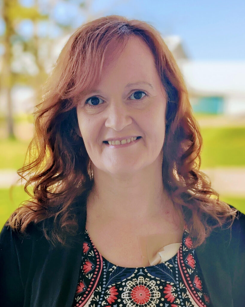 Headshot of Valerie Cober. Valerie is smiling in the sun wearing a patterned shirt and visible chest port.
